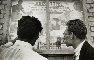 (Two men reading a newspaper board in Germany)